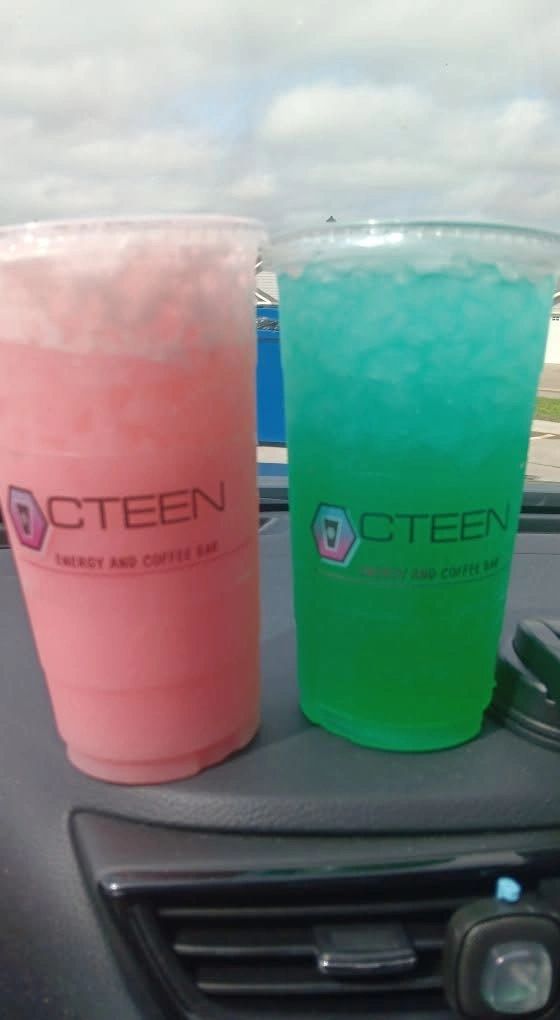Two Octeen CTEEN energy drinks, one pink and one green, on a car dashboard